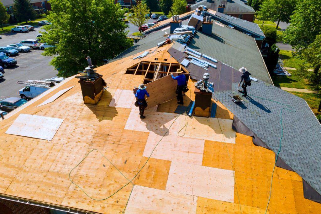 Roofers installing plywood decking as part of the roof replacement process to ensure a sturdy and reliable roof.